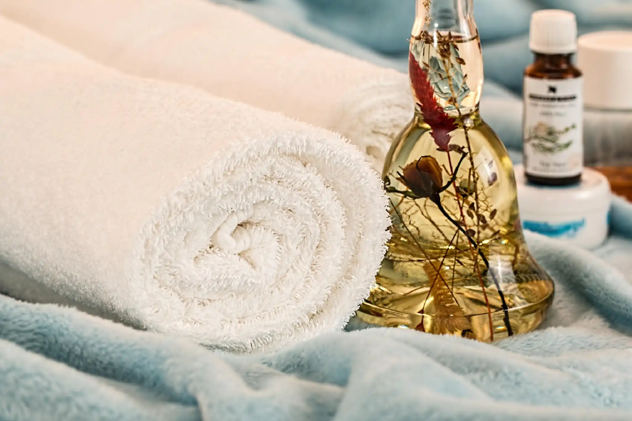 Rolled white towel next to a decorative glass bottle with herbs.