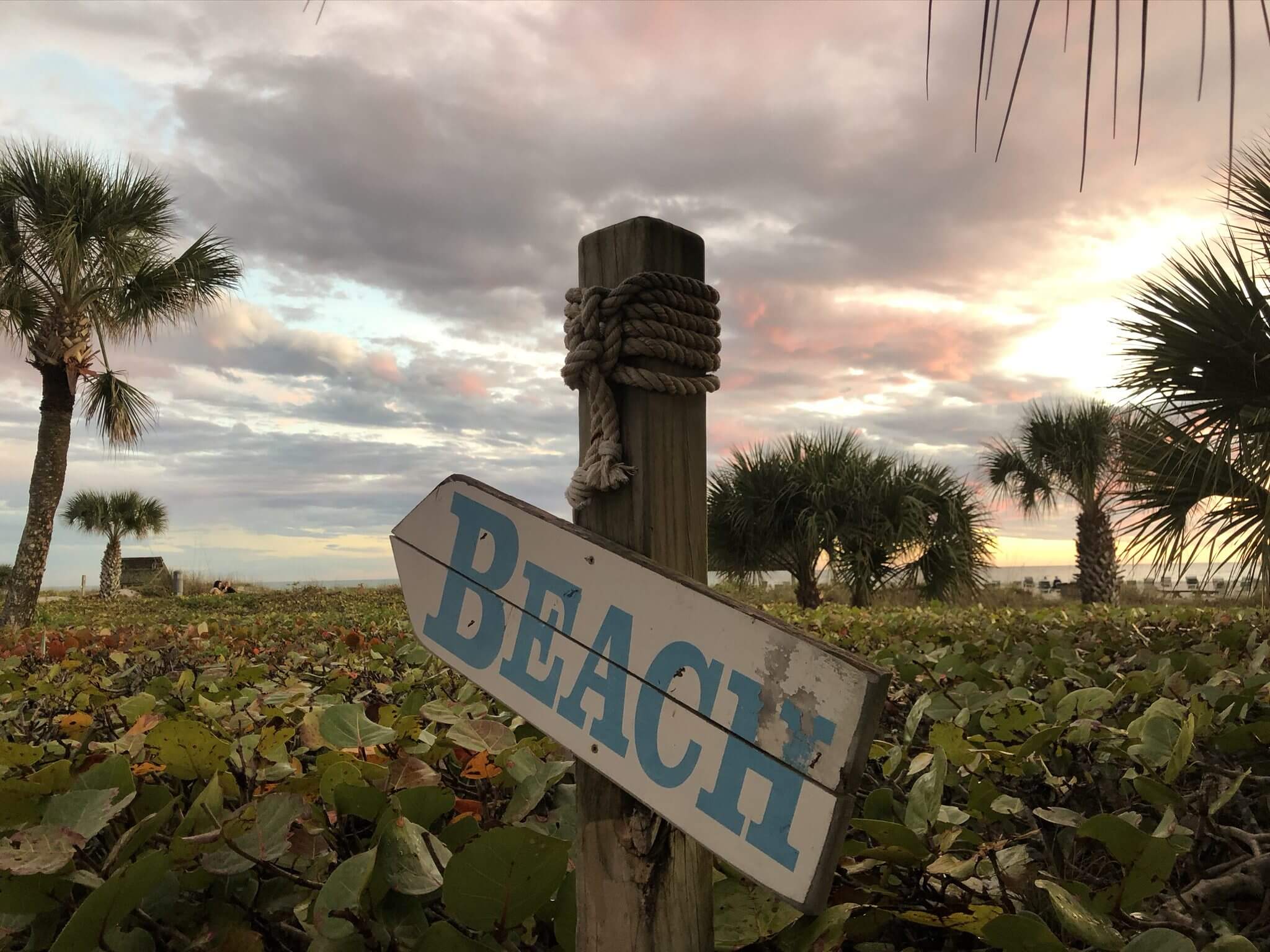 A wooden sign pointing to the beach against a cloudy sky.