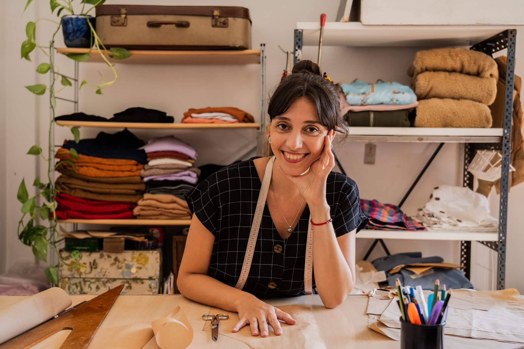 Smiling seamstress sitting at a sewing machine in a cozy workshop.