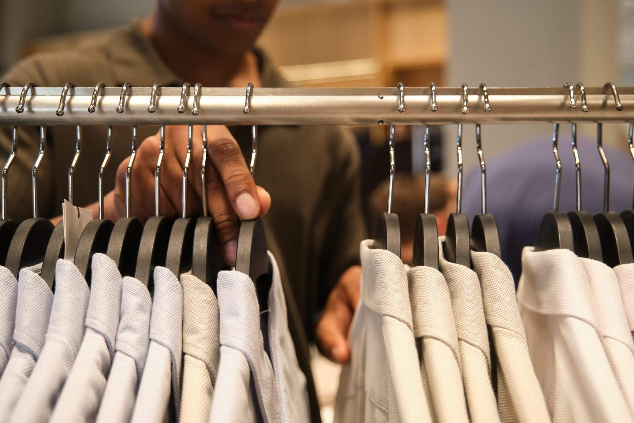 Person browsing shirts on a clothing rack in a store.