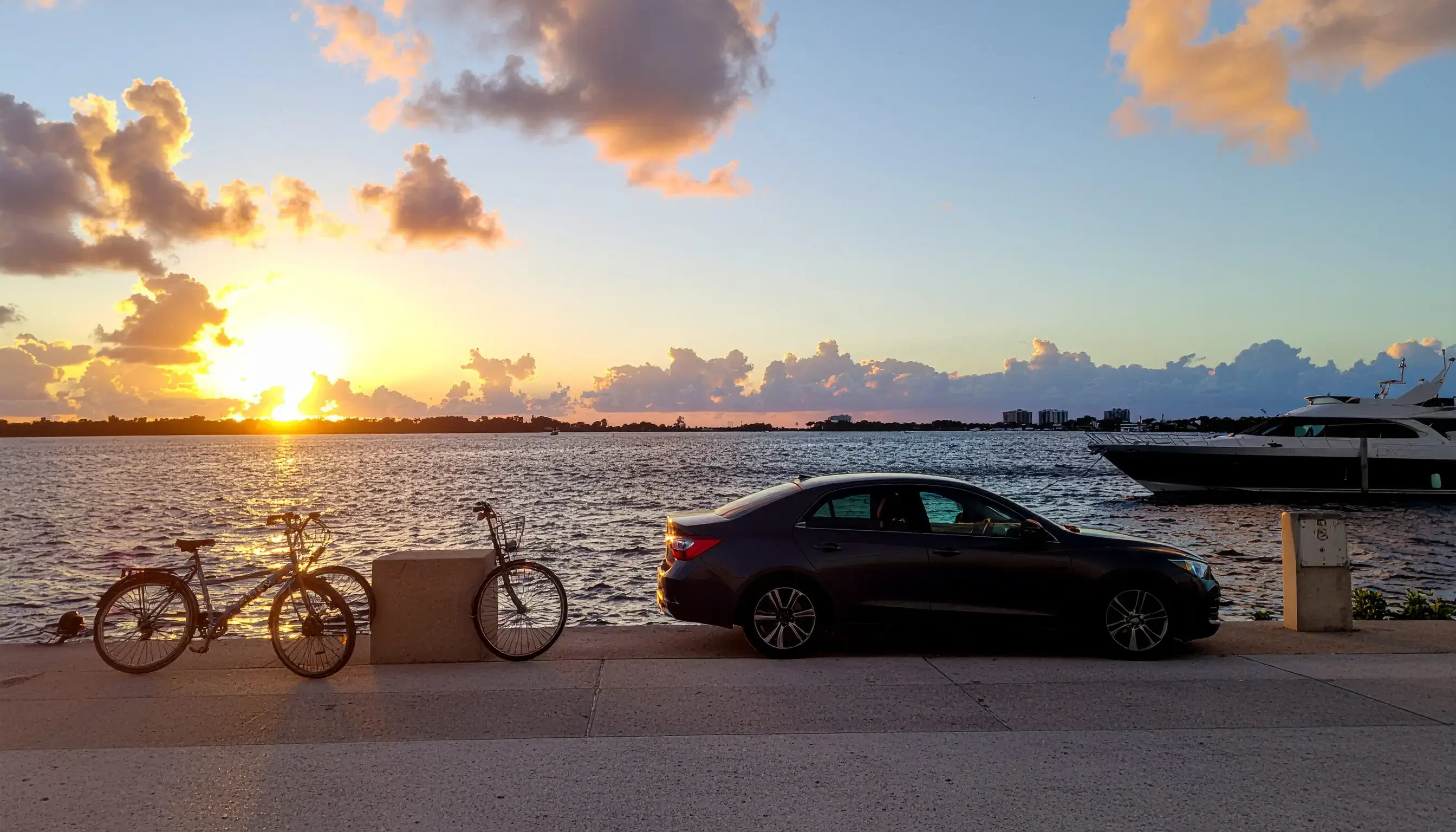 A bicycle and parked car by the waterfront at sunset.