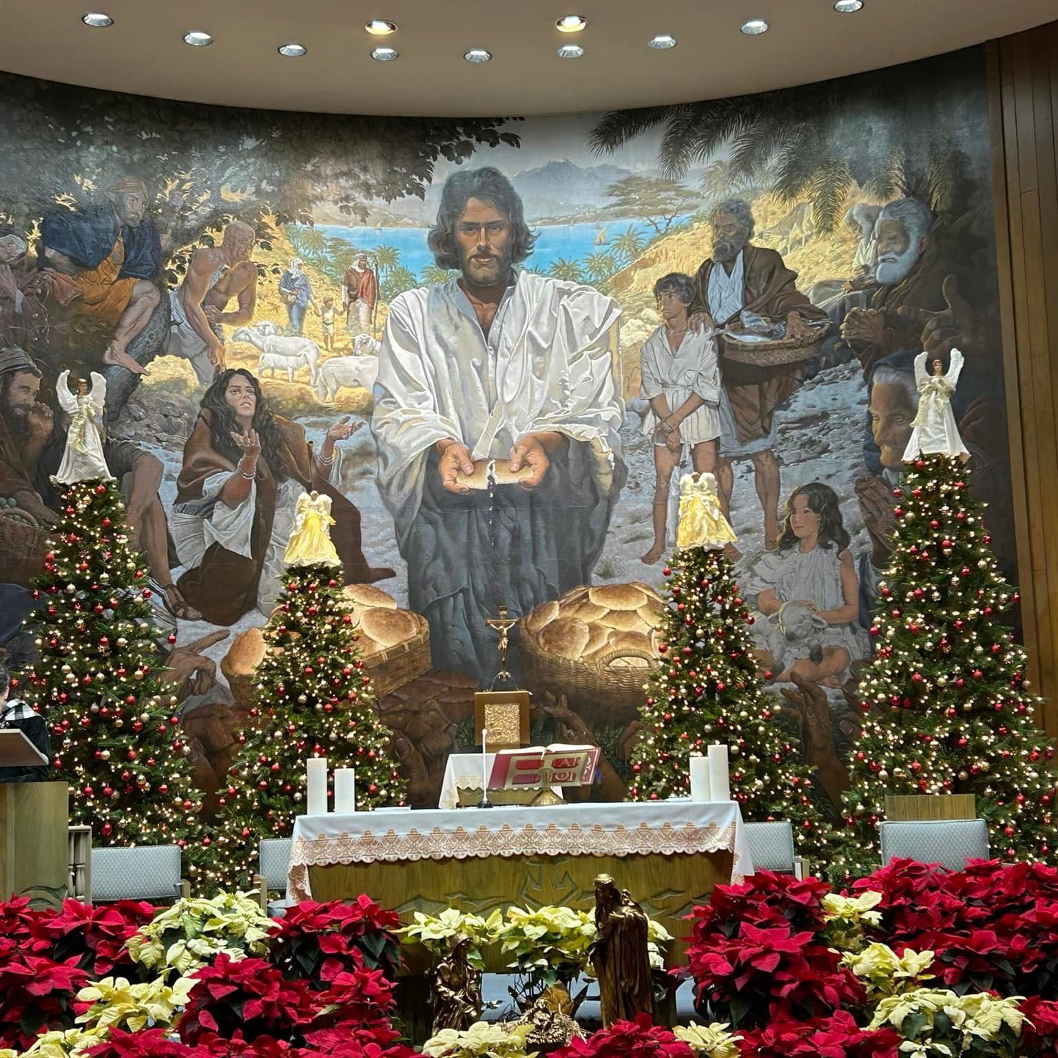 Church altar decorated with Christmas trees and poinsettias under a large religious mural.