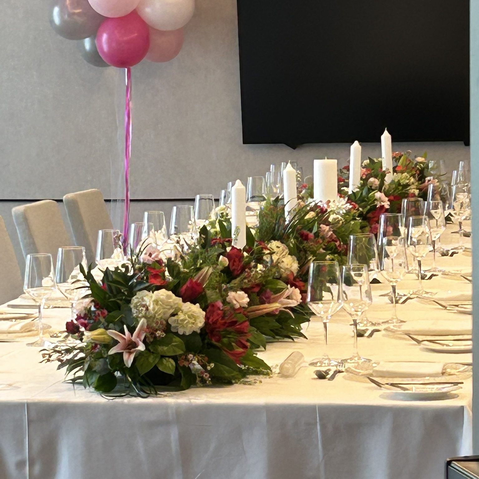 Elegant dining table with floral centerpiece and balloons for celebration.