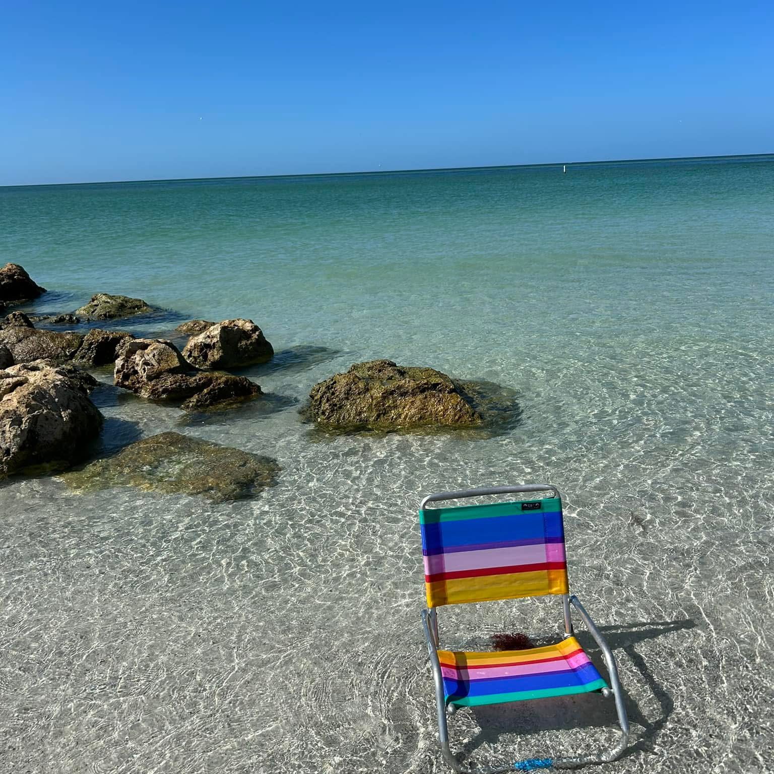 Colorful beach chair on clear sandy shore with rocks and calm sea.