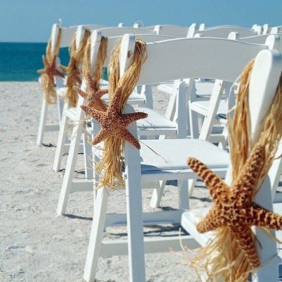 White chairs decorated with starfish and dried grasses on a beach.