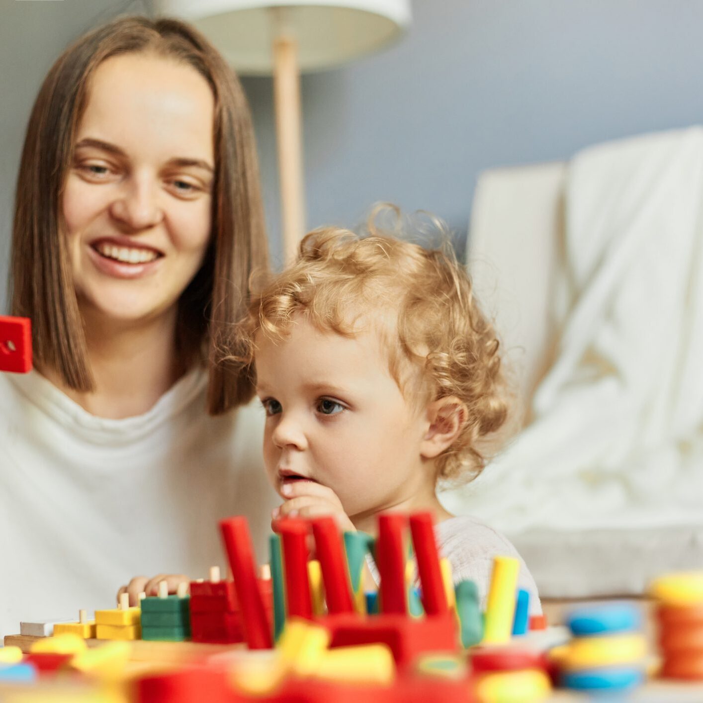 A smiling woman and a child playing with colorful toys indoors.